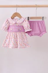 Baby girl's outfit with polka dot dress and pink bloomers on a hanger against a white background